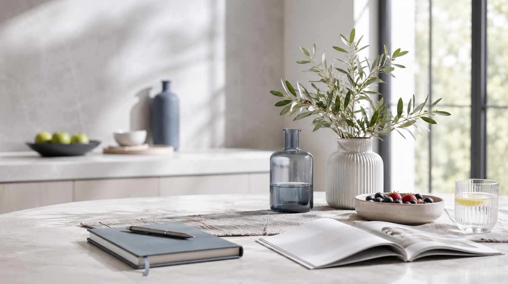 Bright modern wellness setting with fruit, lemon water, notebook and leafy greenery on a marble table.